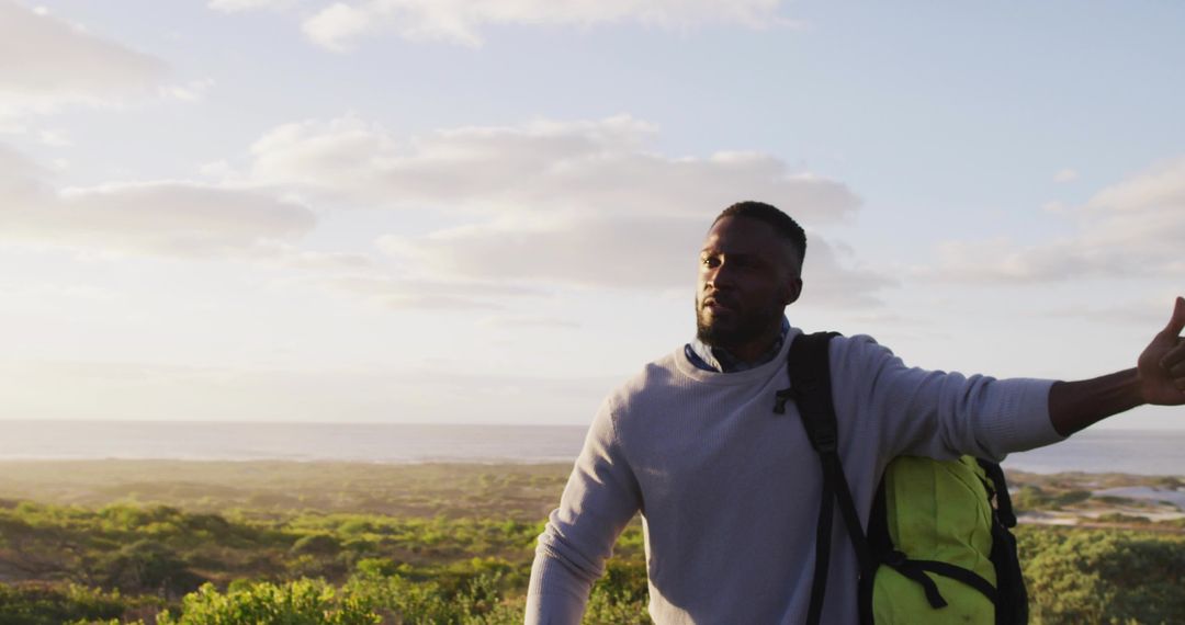 Man Signaling on Coastal Path with Green Backpack and Open Landscape