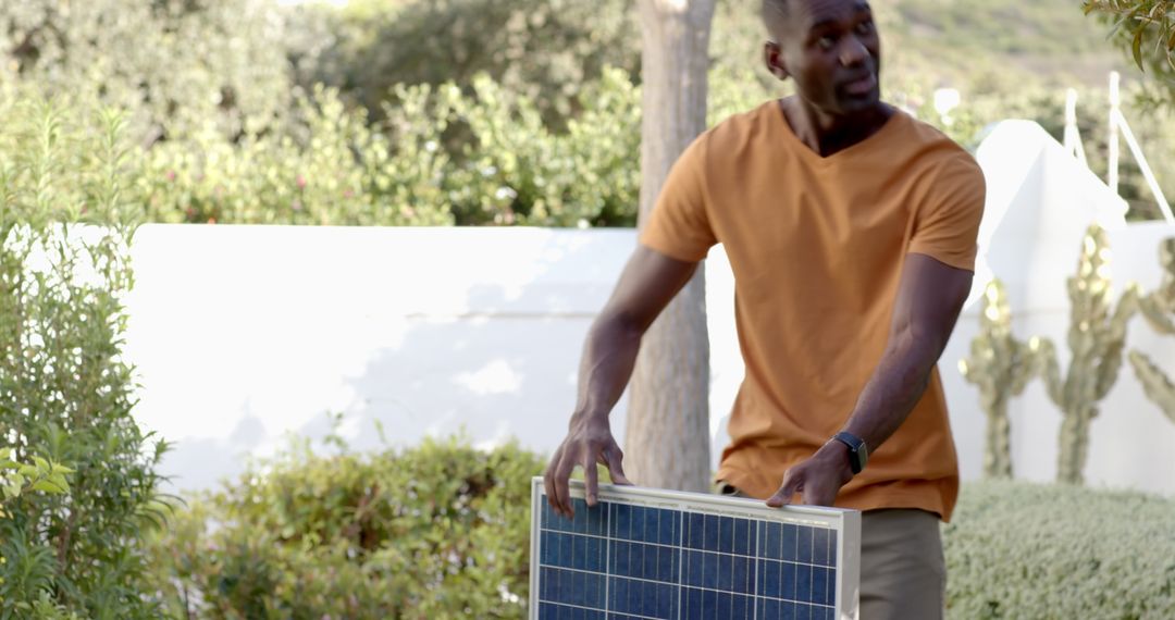 Man Handling Portable Solar Panel in Eco-Friendly Backyard