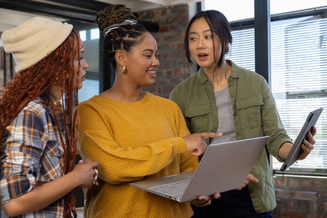 Diverse Female Team Collaborates with Laptop and Tablet in Modern Office