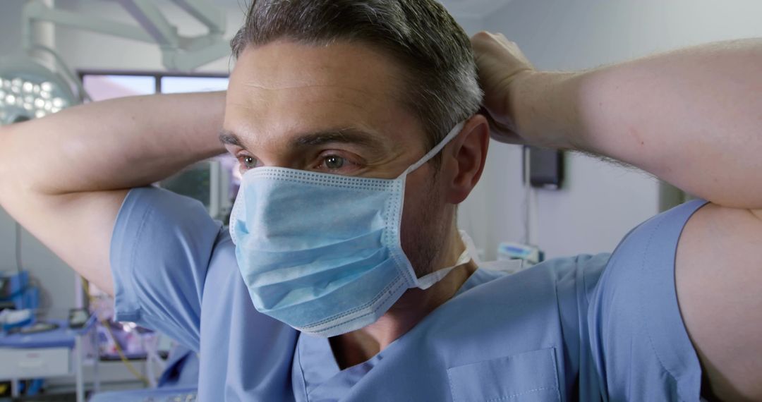 Surgeon Securing Surgical Mask and Preparing for Procedure Under Operating Light