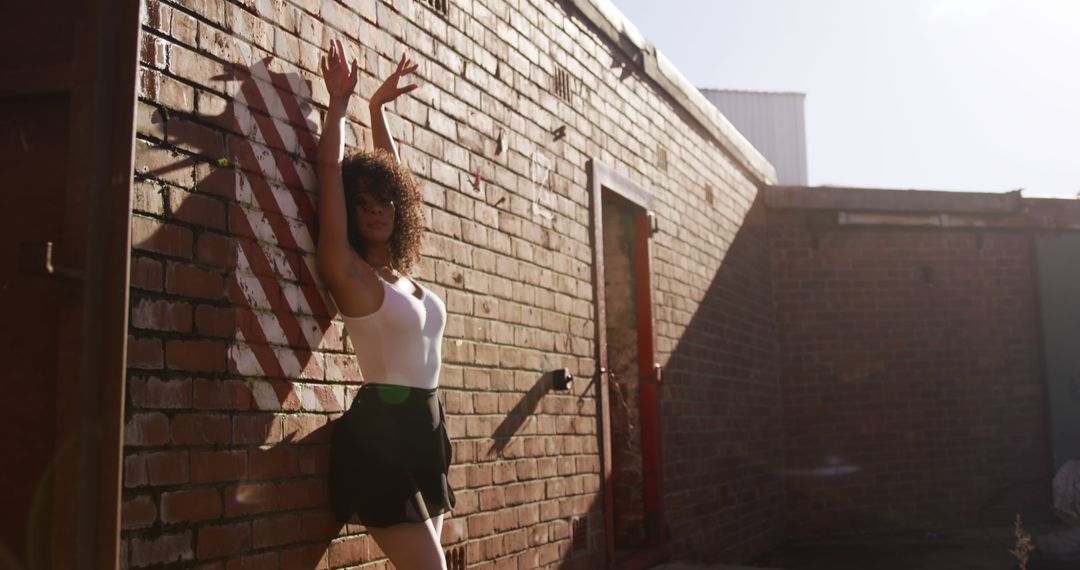 Woman Striking Dance Pose Against Brick Wall in Urban Setting - Free Images, Stock Photos and Pictures on Pikwizard.com