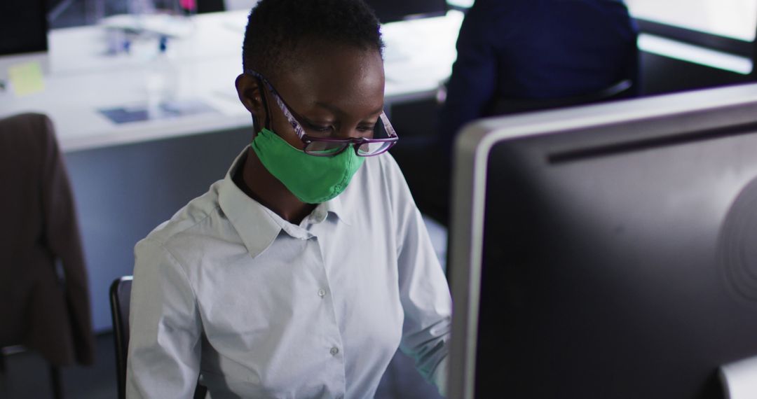 Professional Woman Working on Computer Wearing Green Mask in Office - Free Images, Stock Photos and Pictures on Pikwizard.com