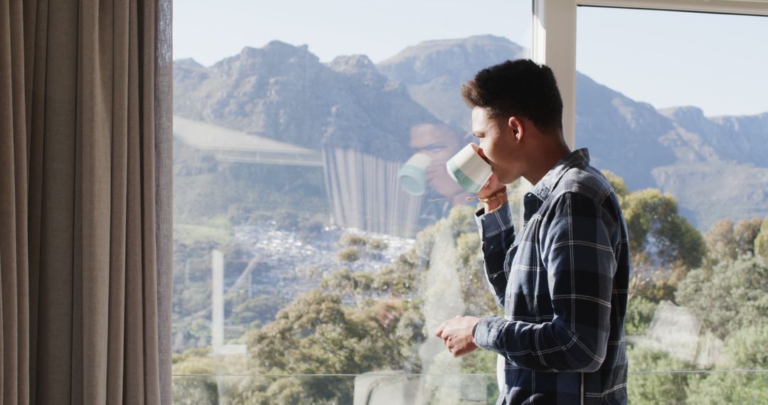 Young man enjoying coffee while looking through window at mountains - Free Images, Stock Photos and Pictures on Pikwizard.com