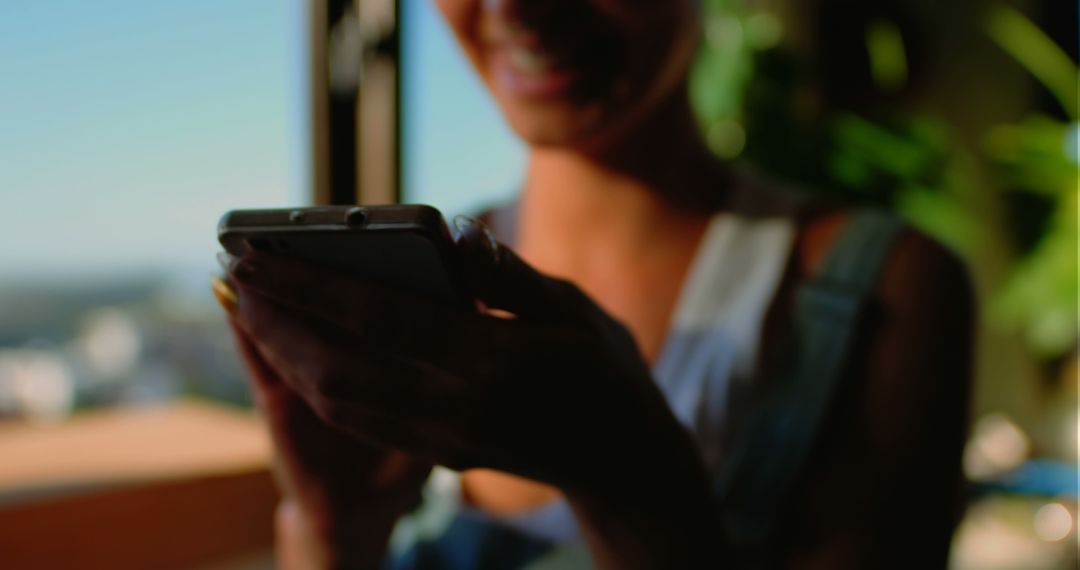 Person Smiling and Texting on Smartphone Near Window - Free Images, Stock Photos and Pictures on Pikwizard.com