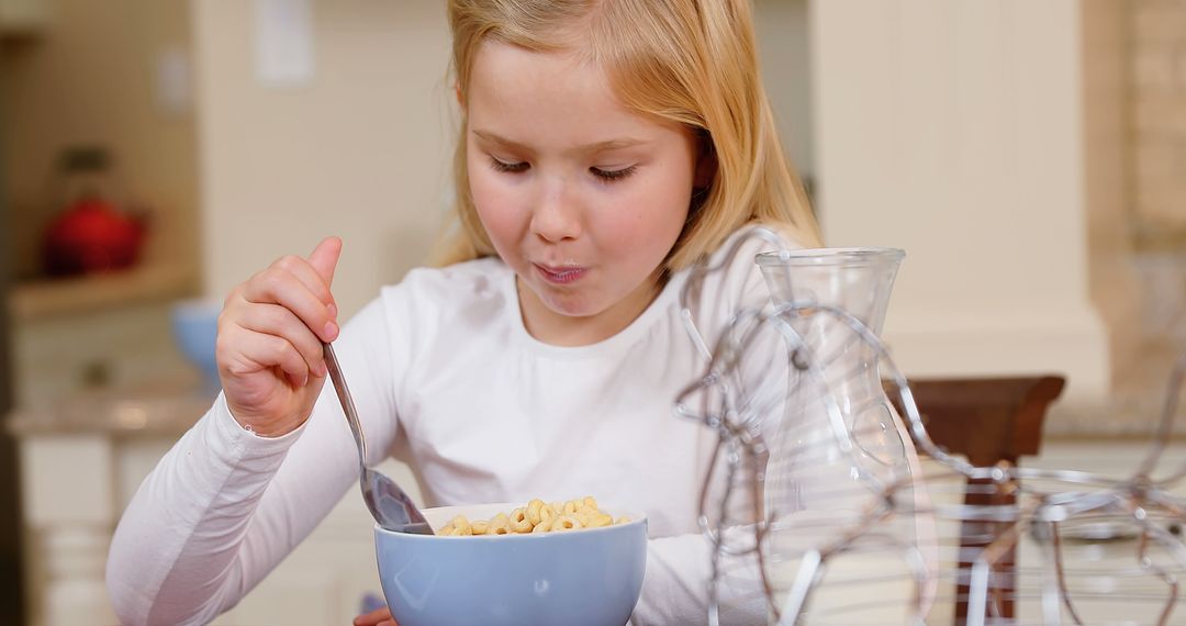 Blonde girl eating breakfast cereal at kitchen table - Free Images, Stock Photos and Pictures on Pikwizard.com