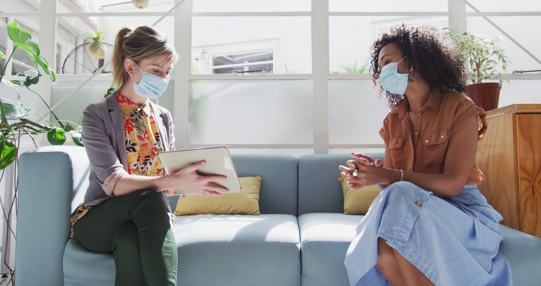 Two Businesswomen Wearing Masks Discussing Plans in Office Setting