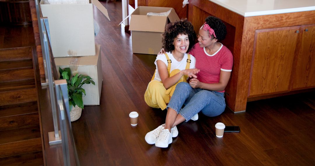 Smiling Lesbian Couple Sitting on Floor Unpacking Boxes at Home
