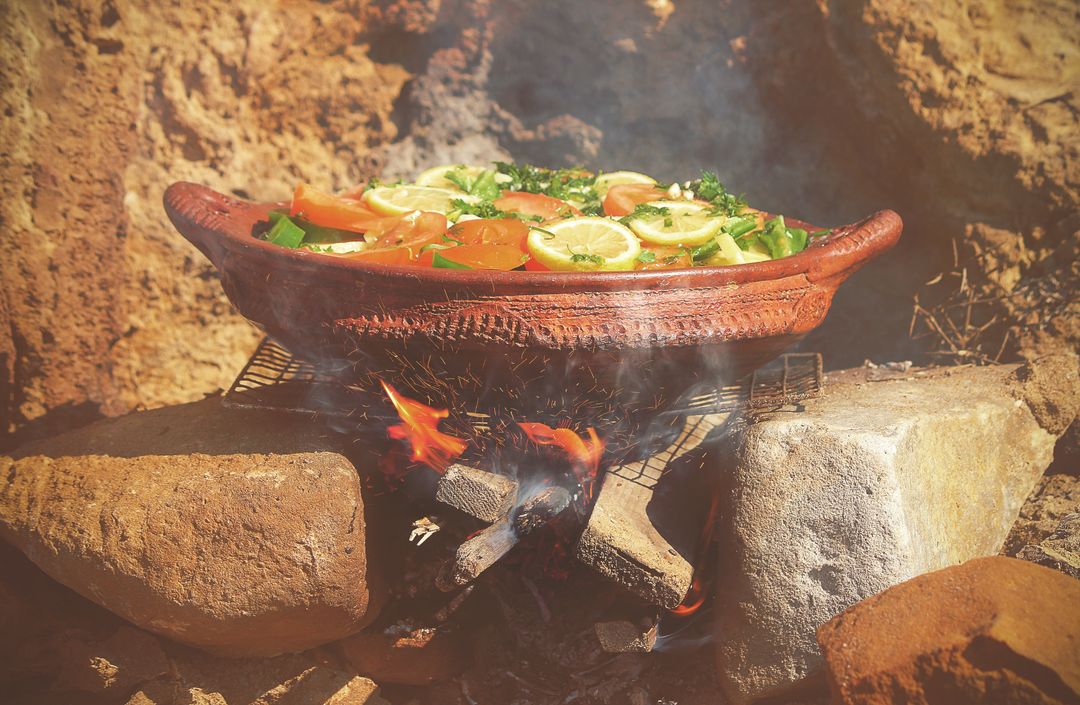 Rustic Clay Pot Cooking Over Open Fire with Lemon Slices, Tomatoes and Fresh Herbs