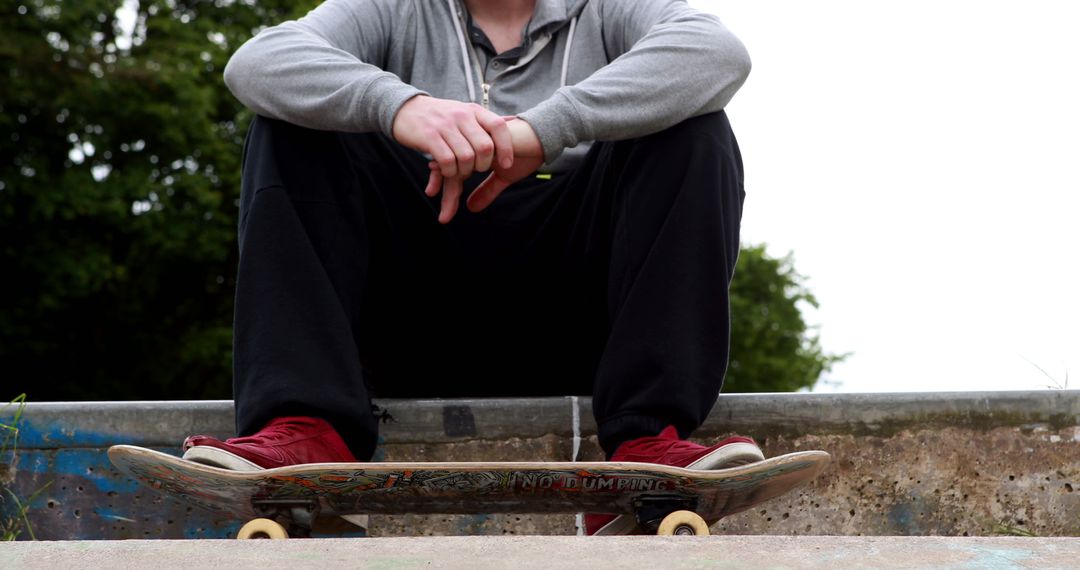 Young Skateboarder Sitting on Skateboard at Skate Park - Free Images, Stock Photos and Pictures on Pikwizard.com