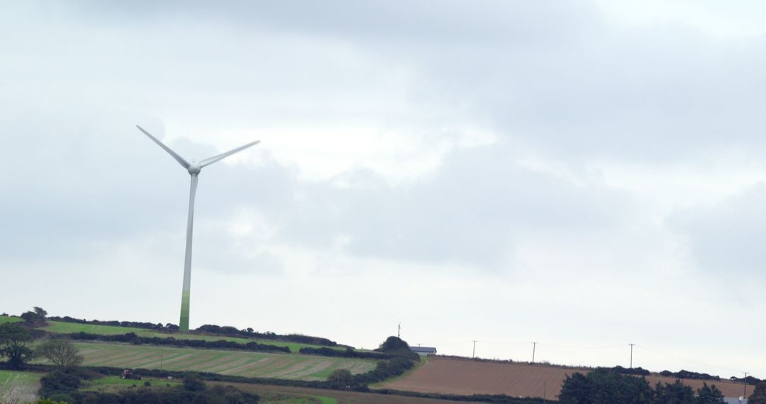 Rural Landscape with Wind Turbine and Cropland Under Cloudy Sky - Free Images, Stock Photos and Pictures on Pikwizard.com