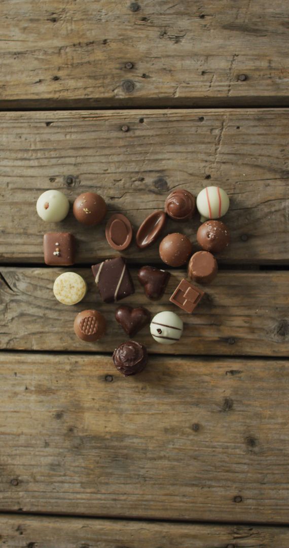 Assorted chocolates forming heart shape on rustic wooden background - Free Images, Stock Photos and Pictures on Pikwizard.com