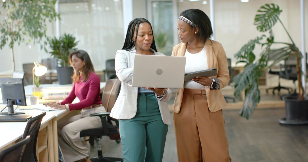 Diverse Women Collaborating with Laptop and Tablet in Modern Open-Plan Office Workspace