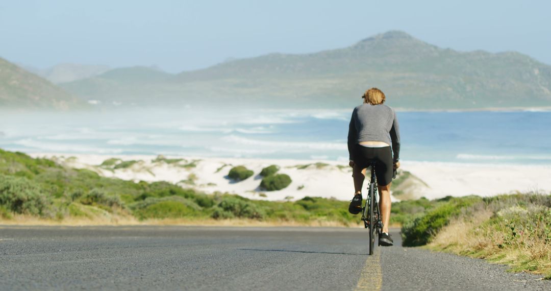 Solo Cyclist Riding Along Coastal Highway with Mountain View - Free Images, Stock Photos and Pictures on Pikwizard.com