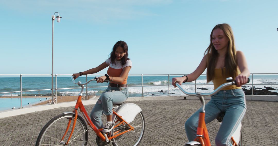 Two young women riding bicycles near seaside on sunny day - Free Images, Stock Photos and Pictures on Pikwizard.com