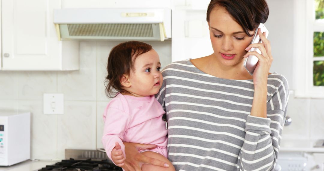 Mother Holding Baby While Talking on Phone in Kitchen - Free Images, Stock Photos and Pictures on Pikwizard.com