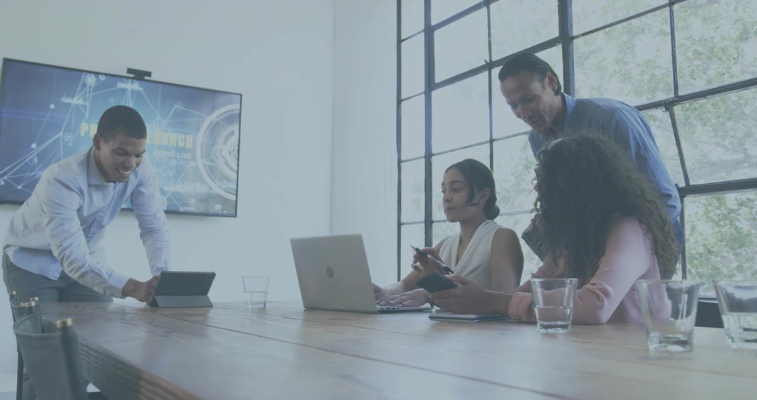 Multicultural team collaborating around conference table with laptop tablet and smartphones