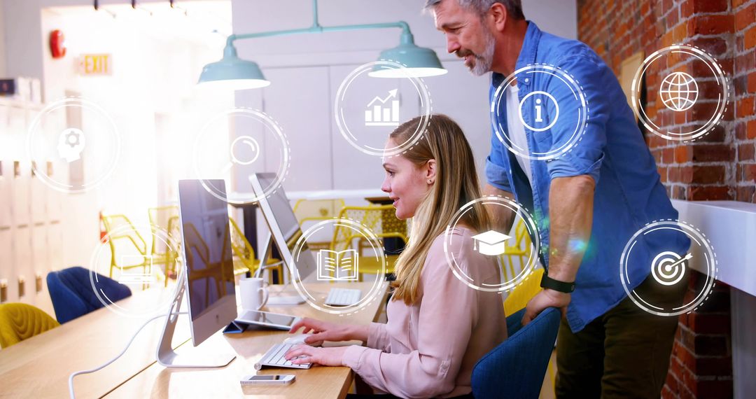 Woman and Mentor Collaborating at Desktop in Modern Open-Plan Office with Digital Icons