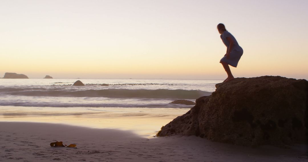 Person Standing on Rock Watching Sunset at Tranquil Beach - Free Images, Stock Photos and Pictures on Pikwizard.com