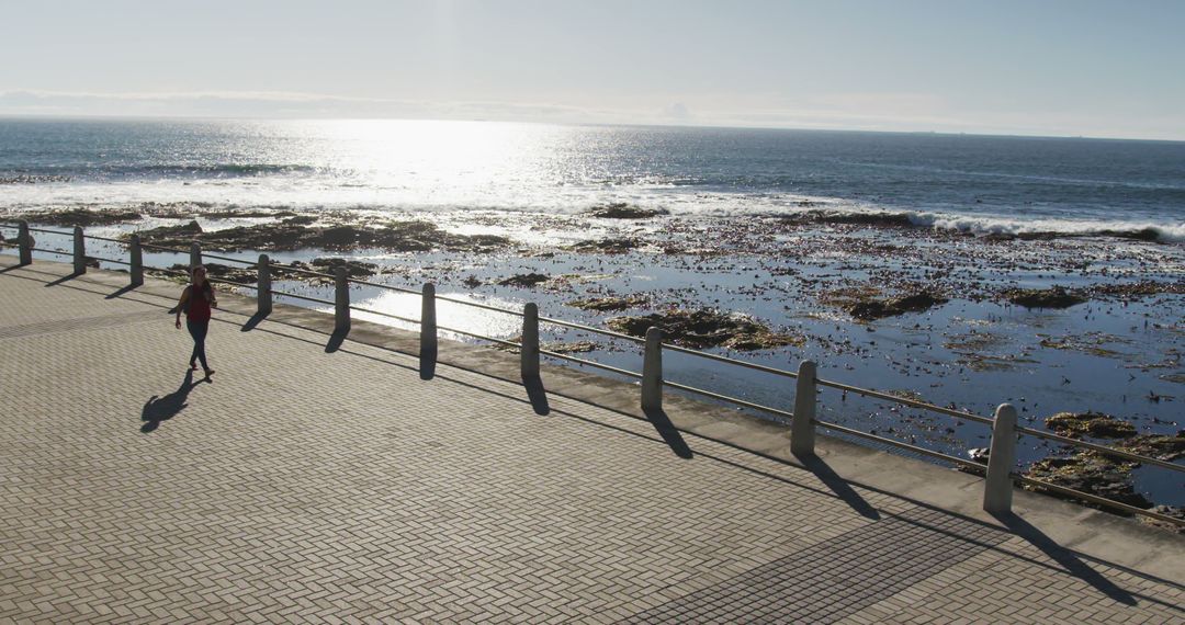 Person Jogging Along Sunny Oceanfront Promenade - Free Images, Stock Photos and Pictures on Pikwizard.com