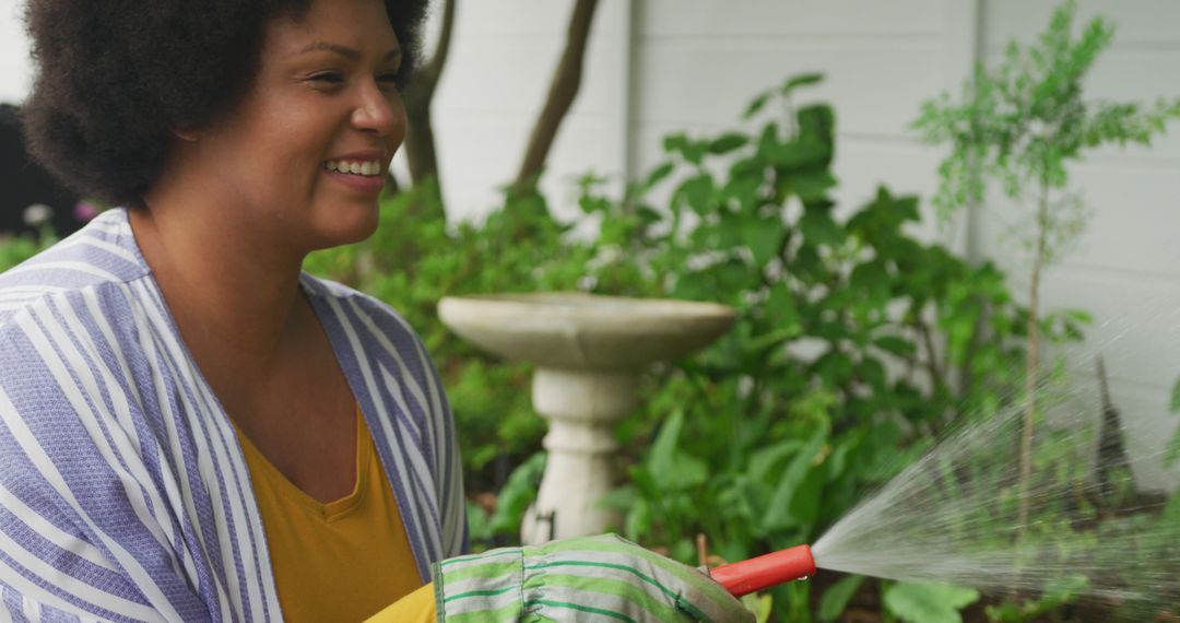 Image of happy plus size african american woman watering flowers in garden - Free Images, Stock Photos and Pictures on Pikwizard.com