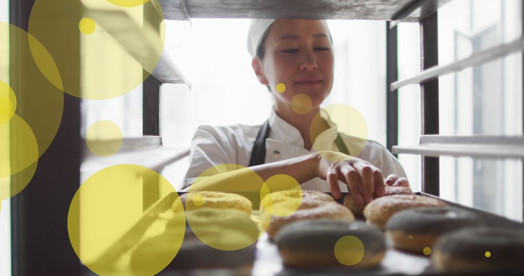 Baker Smiling While Arranging Fresh Donuts on Tray in Bakery Kitchen