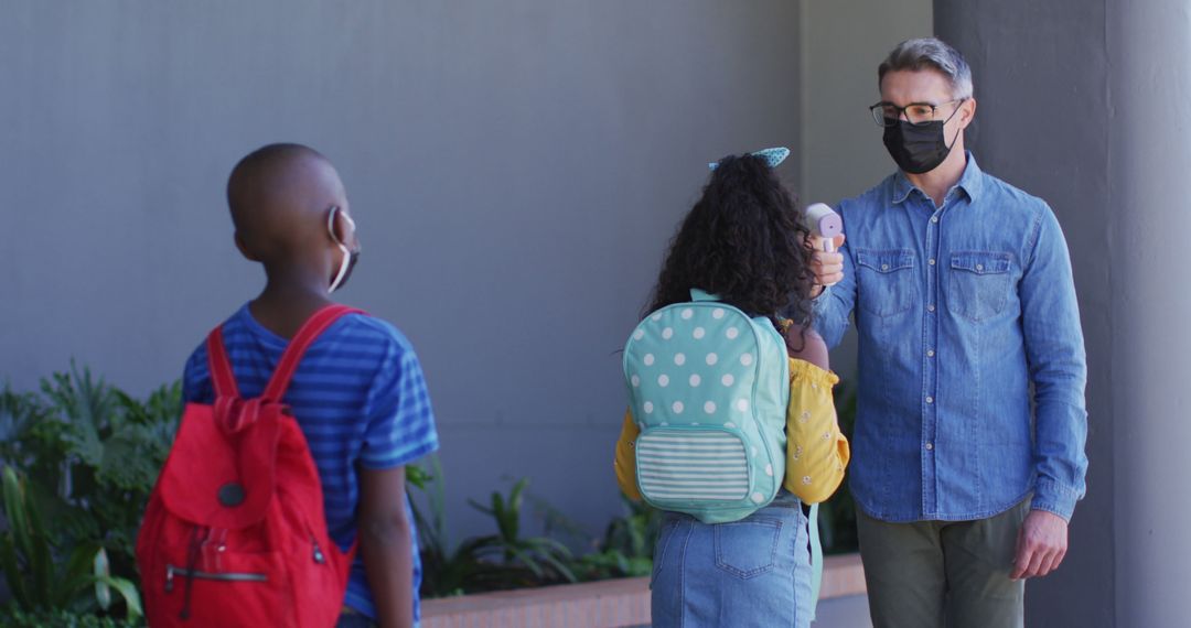 Diverse male teacher measuring temperature of schoolchildren, all wearing face masks - Free Images, Stock Photos and Pictures on Pikwizard.com