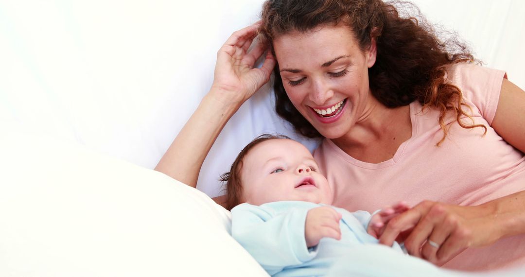 Happy Mother Tickling Infant While Relaxing on Bed at Home