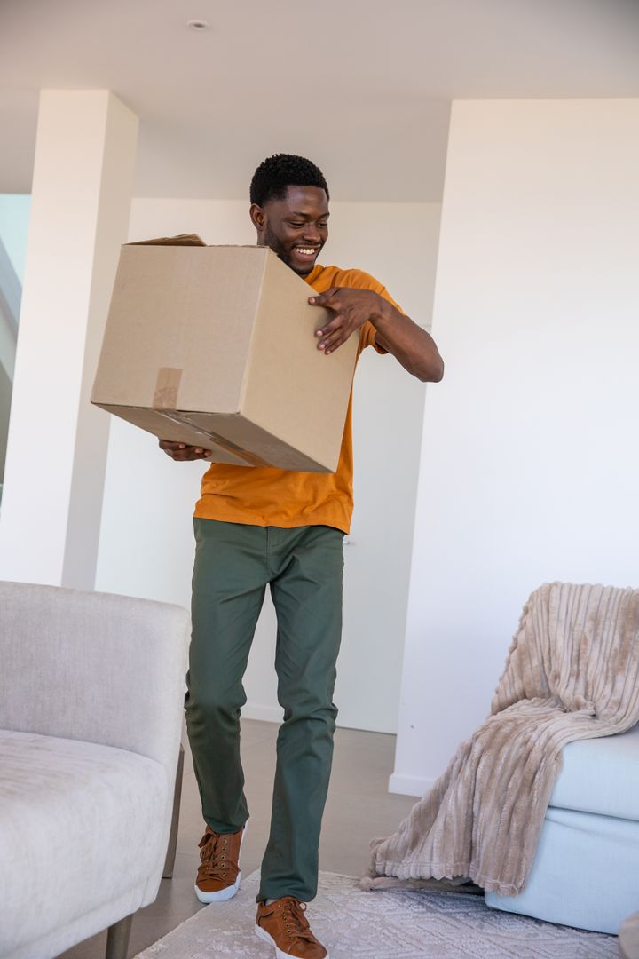 Man Smiling Holding Box in Modern Living Room During Move-In