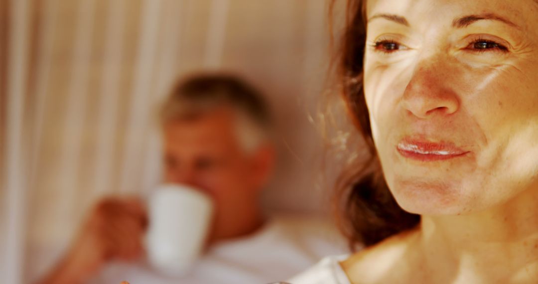 Middle-aged woman reflecting with man drinking coffee in background - Free Images, Stock Photos and Pictures on Pikwizard.com