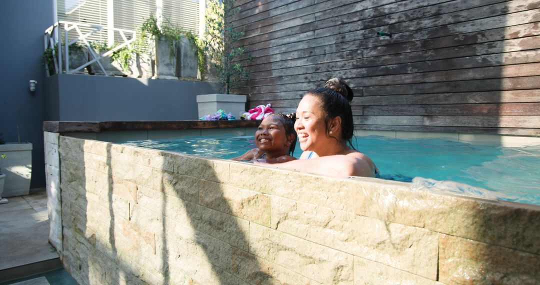Mother and Daughter Relaxing Together by Pool Under Sunlight