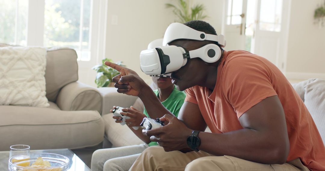 Father Playing VR Headset with Son Holding Game Controllers on Living Room Couch