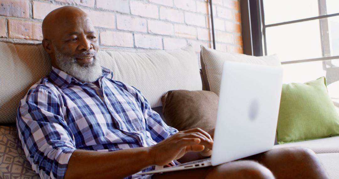 Senior Adult Man Relaxing on Couch Using Laptop in Bright Living Room - Free Images, Stock Photos and Pictures on Pikwizard.com