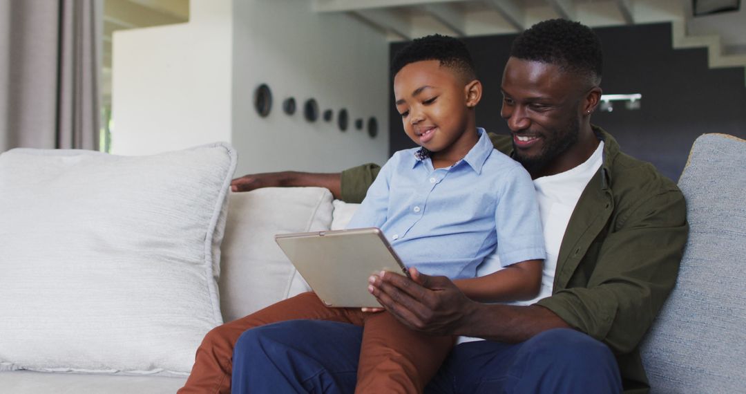 Smiling African American Father and Son Using Tablet on Couch - Free Images, Stock Photos and Pictures on Pikwizard.com