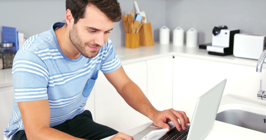 Man Working on Laptop in Modern Kitchen Using Smartphone - Free Images, Stock Photos and Pictures on Pikwizard.com