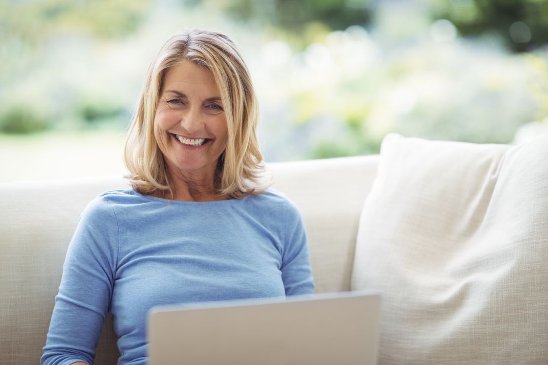 Smiling senior woman sitting on sofa with laptop in living room - Free Images, Stock Photos and Pictures on Pikwizard.com