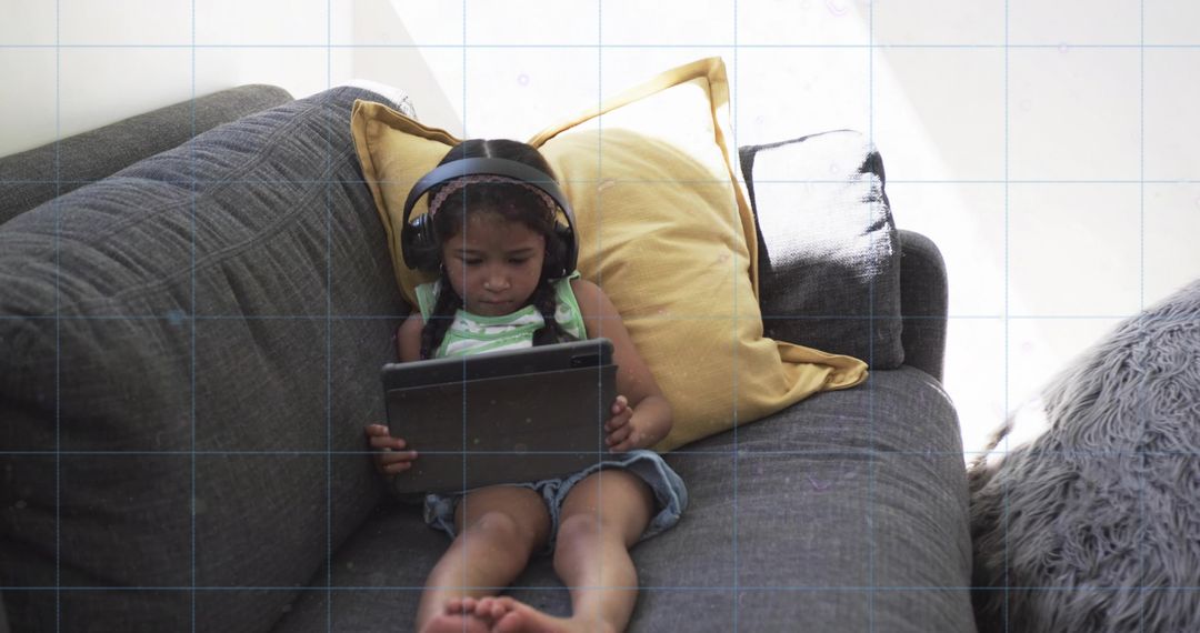 Child Listening on Tablet While Relaxing on Grey Sofa with Mustard Pillow