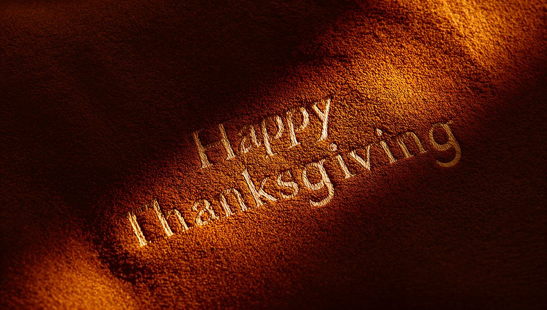 Glowing embossed Happy Thanksgiving on warm suede leather with dramatic directional light