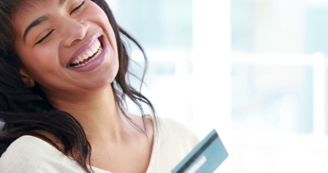 Laughing Woman Holding Credit Card Indoors with Bright Background - Free Images, Stock Photos and Pictures on Pikwizard.com