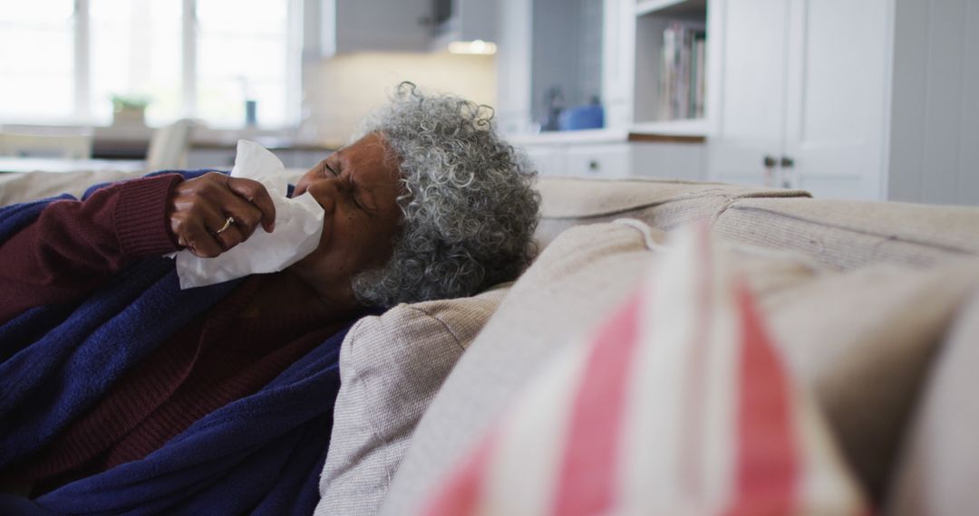 Senior woman sneezing into tissue while lying on couch at home - Free Images, Stock Photos and Pictures on Pikwizard.com