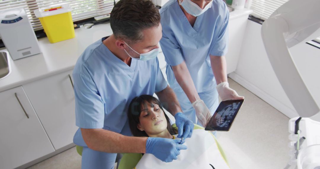 Dentists Reviewing Dental X-Ray on Tablet While Examining Patient in Clinic
