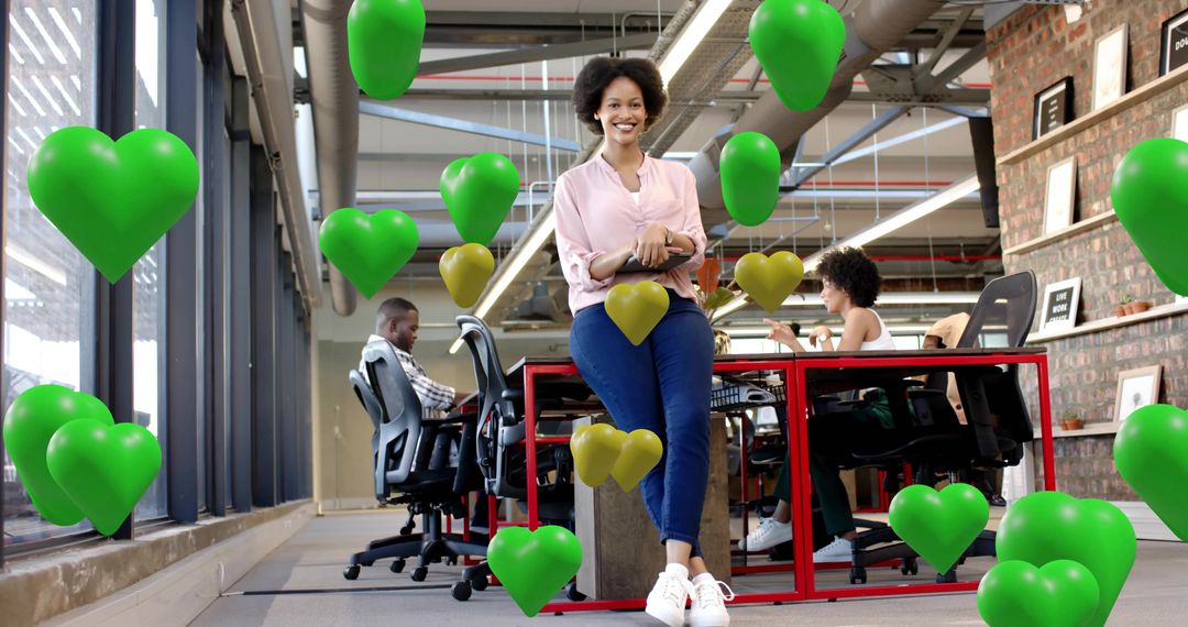 Smiling professional holding tablet leaning on desk in modern coworking with green heart balloons