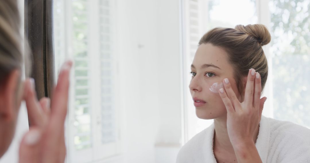 Young Woman Applying Cream to Face in Bathroom Mirror - Free Images, Stock Photos and Pictures on Pikwizard.com