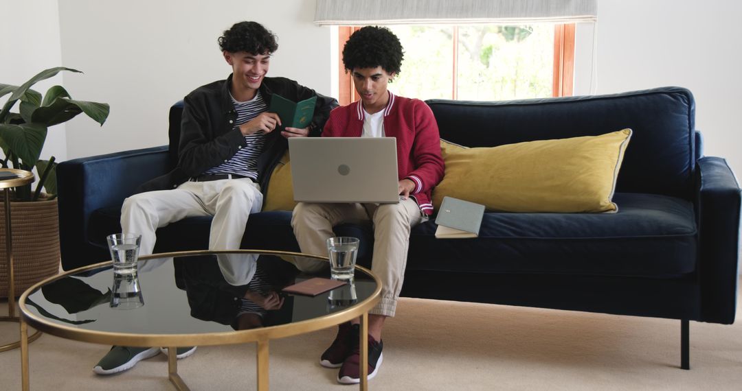 Two friends sharing laptop on navy sofa in modern living room, collaborating on project