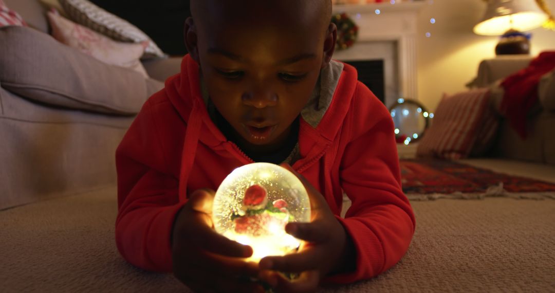 Curious Boy Holding Glowing Christmas Ornament Indoors - Free Images, Stock Photos and Pictures on Pikwizard.com