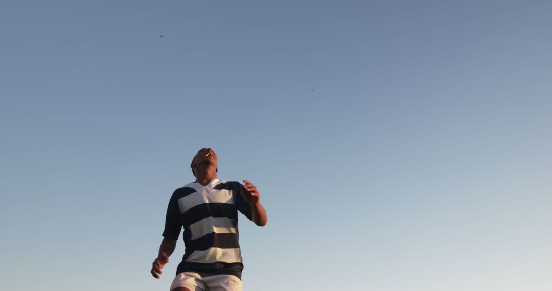 Man in striped rugby shirt looking upwards against clear sky - Free Images, Stock Photos and Pictures on Pikwizard.com