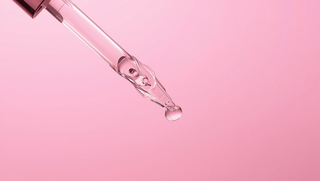 Glass Dropper Pipette Creating Droplet on Pink Background