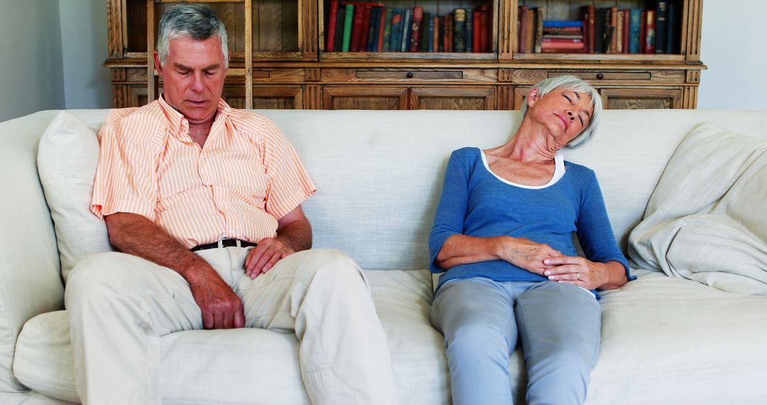 Older Couple Sleeping on Sofa at Home with Bookshelf