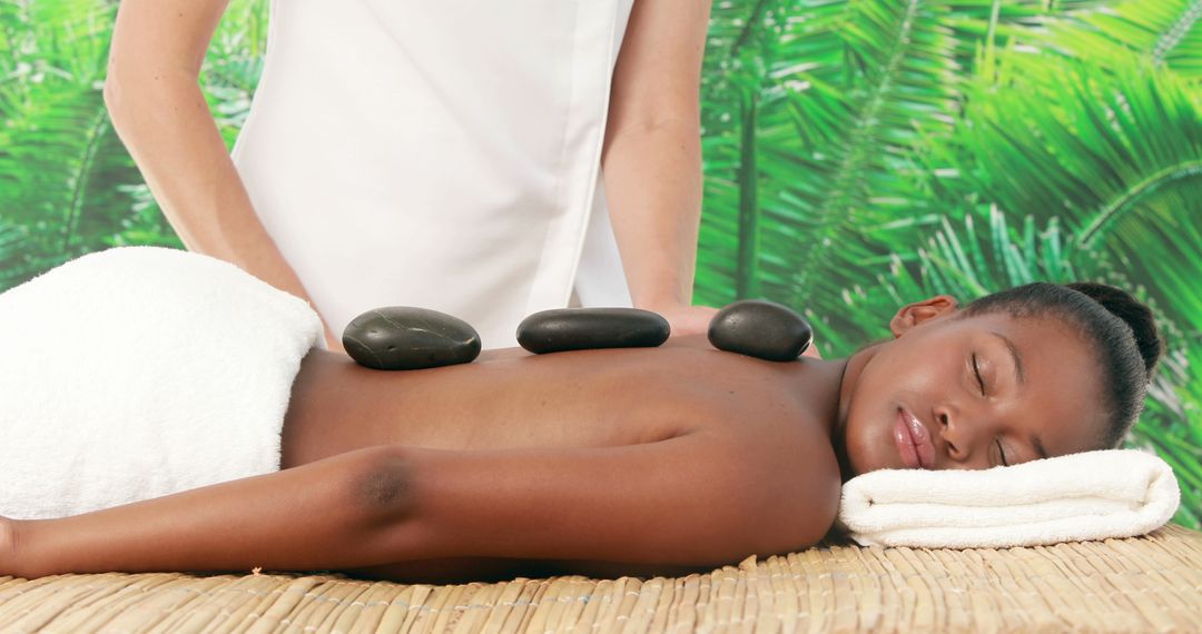 An African American woman enjoys a relaxing hot stone massage at a spa, with copy space - Free Images, Stock Photos and Pictures on Pikwizard.com