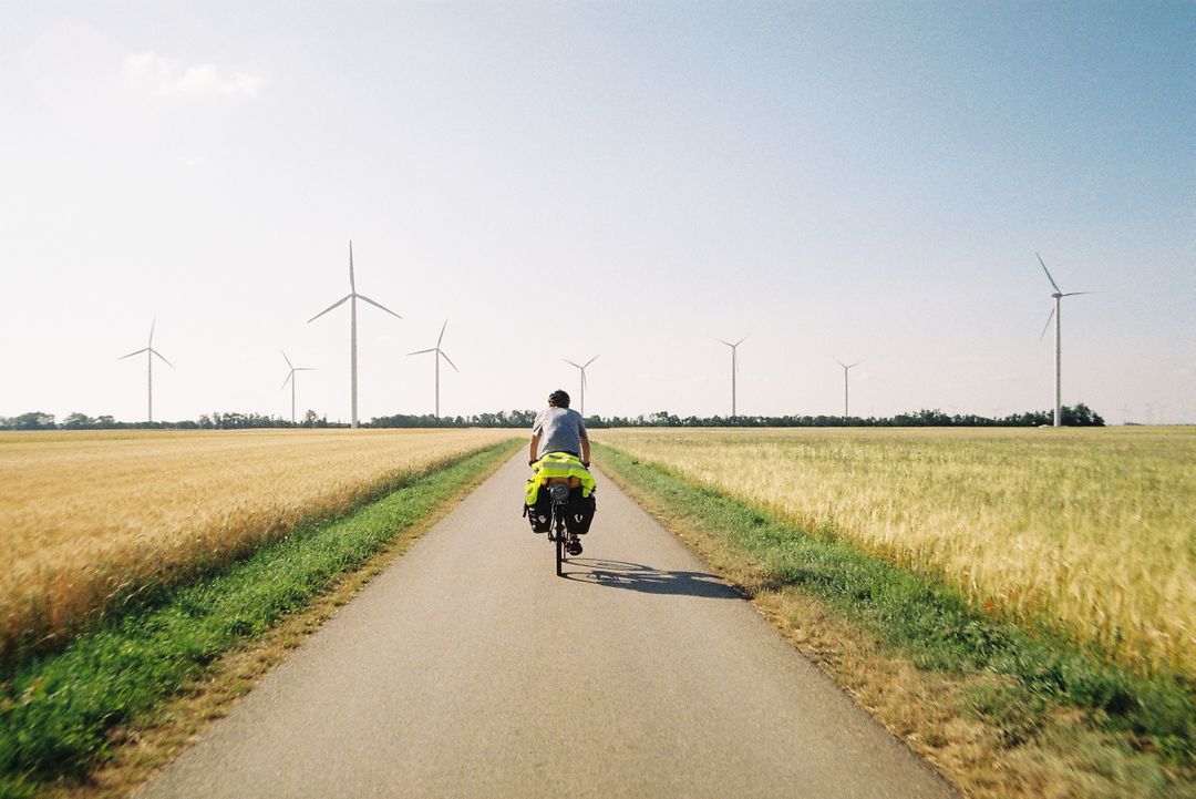 Cyclist Enjoying Ride on Country Road with Wind Turbines in Background - Free Images, Stock Photos and Pictures on Pikwizard.com