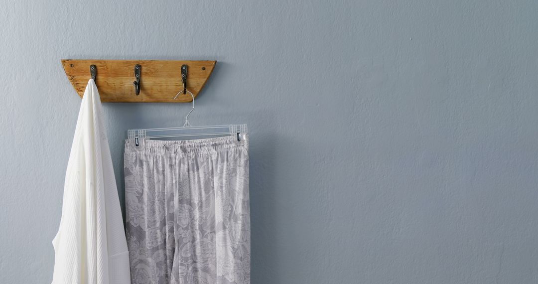 A minimalist wooden coat rack with metal hooks displays a towel and pants on a blue wall. - Free Images, Stock Photos and Pictures on Pikwizard.com